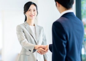 写真:人材採用のイメージ。スーツ姿の女性が企業の担当者と握手をしている。