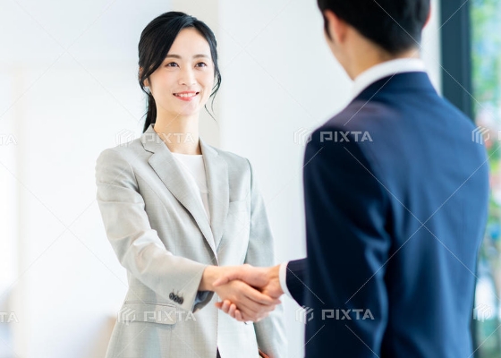 写真:人材採用のイメージ。スーツ姿の女性が企業の担当者と握手をしている。